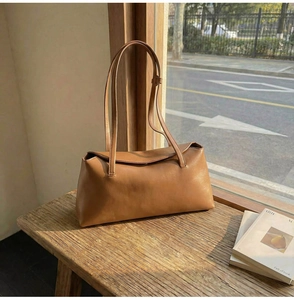 Detail of tan brown PU leather shoulder bag with sleek flap and slim straps on wooden stool