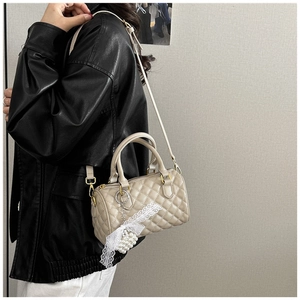 Detail of beige quilted Boston bag with lace pearl charm and adjustable strap worn by model