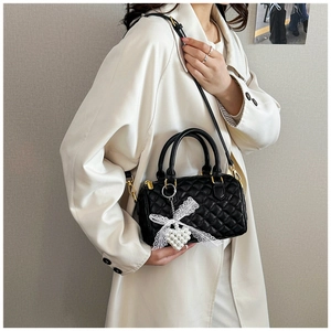 Quilted black Boston handbag with lace bow and pearl charm detail shown on a trench coat