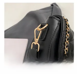 Close-up of golden metal hook and chain strap on black quilted leather saddle bag