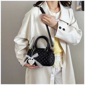 Detail of black quilted Boston bag with lace heart charm and pearl accessories