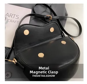 Detail view of the black saddle bag showing dual golden magnetic snaps and matte leather