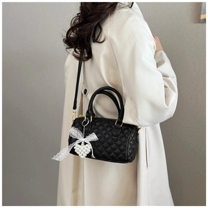 Close-up of black quilted boston bag with pearl heart charm and lace bow details