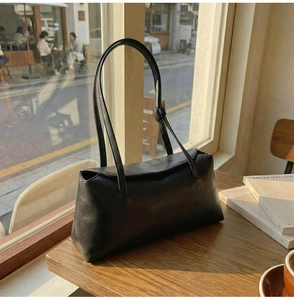 Detail of a black rectangular faux leather shoulder bag on a cafe table in soft sunlight
