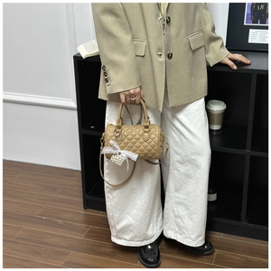 Close-up of khaki quilted Boston bag with pearl heart lace charm and leather handle