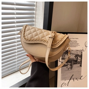 Detail of beige saddle bag featuring quilted pattern and golden metal chain trim