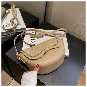 Detail of beige quilted saddle bag featuring a gold chain and faux leather texture