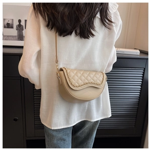 Close-up of beige quilted saddle bag with gold chain strap on model in casual outfit