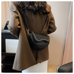 Detail of black quilted saddle bag with gold chain trim and adjustable leather strap