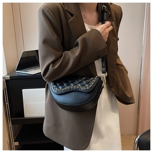 Close-up of black quilted saddle bag with gold chain detail worn by a model in a modern office