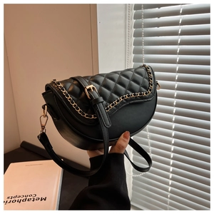 Detail of black quilted saddle bag with gold chain and leather strap held by a person