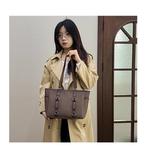 Detail shot of brown herringbone tote bag with dark handles held by model in trench coat