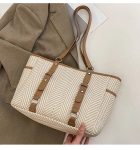 Detail of herringbone weave tote bag with brown leather trim and metal ring accents