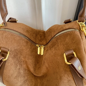 Detailed close-up of dual golden zippers and premium brown suede texture on a tote bag
