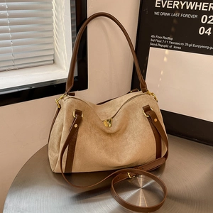 Detail of suede tote bag with leather trim and gold hardware on a modern table
