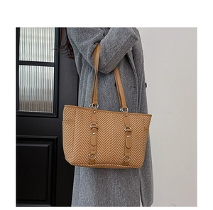Detail of a large woven tote bag with herringbone pattern and brown leather straps