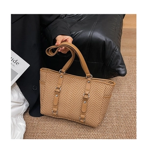 Close-up of brown woven tote bag featuring herringbone pattern and silver rivet details