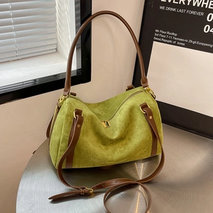 Detail of green suede handbag featuring brown leather handles and gold metal hardware