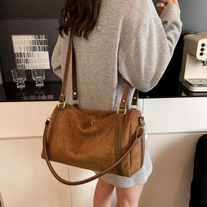 Detail of a dark brown suede cylindrical handbag with leather straps and gold hardware