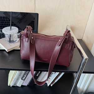 Retro burgundy cylindrical pillow bag with gold hardware on an office shelf setting