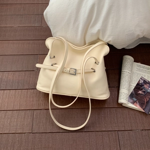 Bolso tote plisado beige minimalista con hebilla plateada en suelo de madera y revista