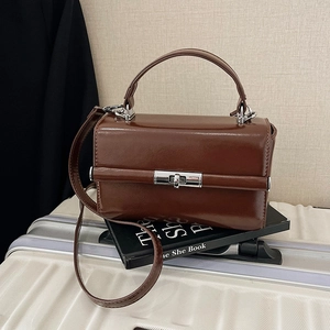 Sac à main vintage marron avec fermoir argenté sur valise blanche et décor de livre