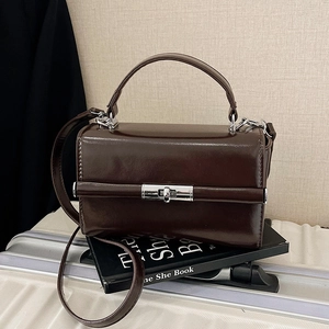 Sac à main rétro en cuir marron foncé avec fermoir argenté sur valise grise