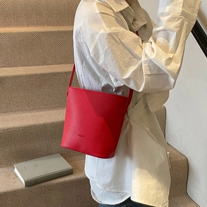 Detail of red lychee textured bucket bag worn by model on a white shirt