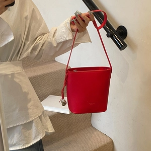 Detail of red bucket bag in lychee leather with heart charm pendant on side