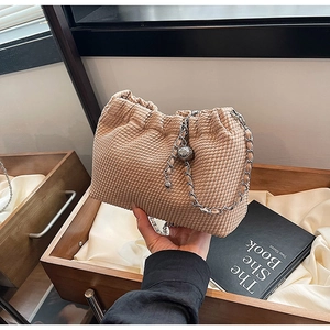 Detail of beige drawstring crossbody bag with silver chain strap and quilted texture
