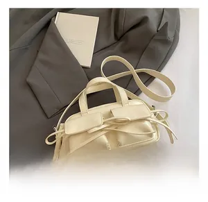 Detail of a beige fashion handbag featuring dual pockets and an elegant bow ribbon decoration