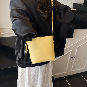 Detailed view of yellow lychee grain leather bucket bag against a black and white outfit