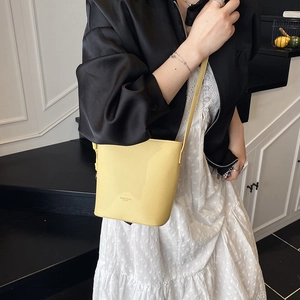 Detail of bright yellow bucket bag in textured leather worn with a stylish outfit