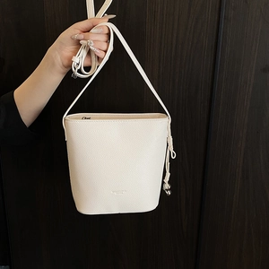 Detail of cream bucket bag in lychee leather featuring a knot charm and a shoulder strap