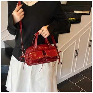 Deep red patent leather handbag featuring bow detail and dual front pockets
