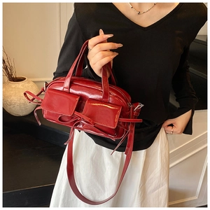 Detail of red patent leather pillow bag with twin pockets, bow accent, and glossy finish