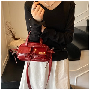 Close-up of wine red patent leather handbag with bow details and long shoulder strap