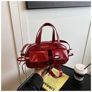 Close-up of red patent leather handbag featuring decorative bows and dual front pockets