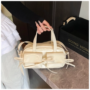 Detail of cream white handbag featuring dual front pockets and decorative ribbon straps