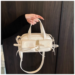 Detail of cream glossy PU handbag with bow accents and functional front pockets