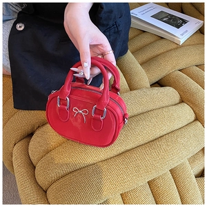 Detail der roten Mini-Handtasche mit silberner Schleife und glänzendem Finish auf gelbem Stoff