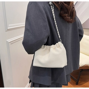 Detail of white pleated shoulder bag with a woven metal chain strap on a model