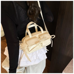 Close-up of cream bow-knot shoulder bag in glossy synthetic leather worn by a model