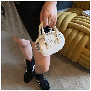 Detail einer weißen Mini-Handtasche mit Metallschleife und Ledertextur aus der Nähe