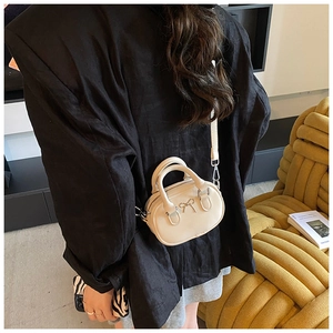 Detail einer cremeweißen Mini-Handtasche mit Metallschleife auf schwarzem Blazer