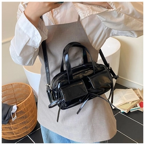 Detail of glossy black handbag featuring bow-tied ribbons and twin front flap pockets