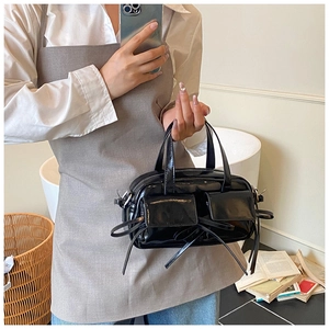 Close-up of black patent leather handbag featuring twin front flap pockets and bow detail