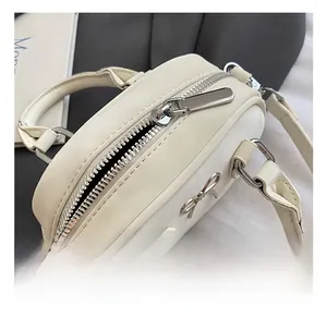 Nahaufnahme von silbernem Reißverschluss und Metallschleife an weißer Mini-Handtasche