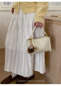 Close-up of white leather handbag with litchi texture and cute monster plush charm