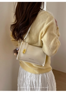 Detail of cream crossbody bag with lychee texture, gold lock and plush pendant charm